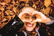 Little girl covered in fallen autumn leaves, holds hands on eyes like binoculars, one eye looking through heart shaped fingers. Leather jacket sleeves. Close-up photography.; Shutterstock ID 1216455229; Purchase Order: Purchase Order No: 410750/512593; Job: 512593; Client/Licensee: Westpac Group; Other: Douglas McIntosh